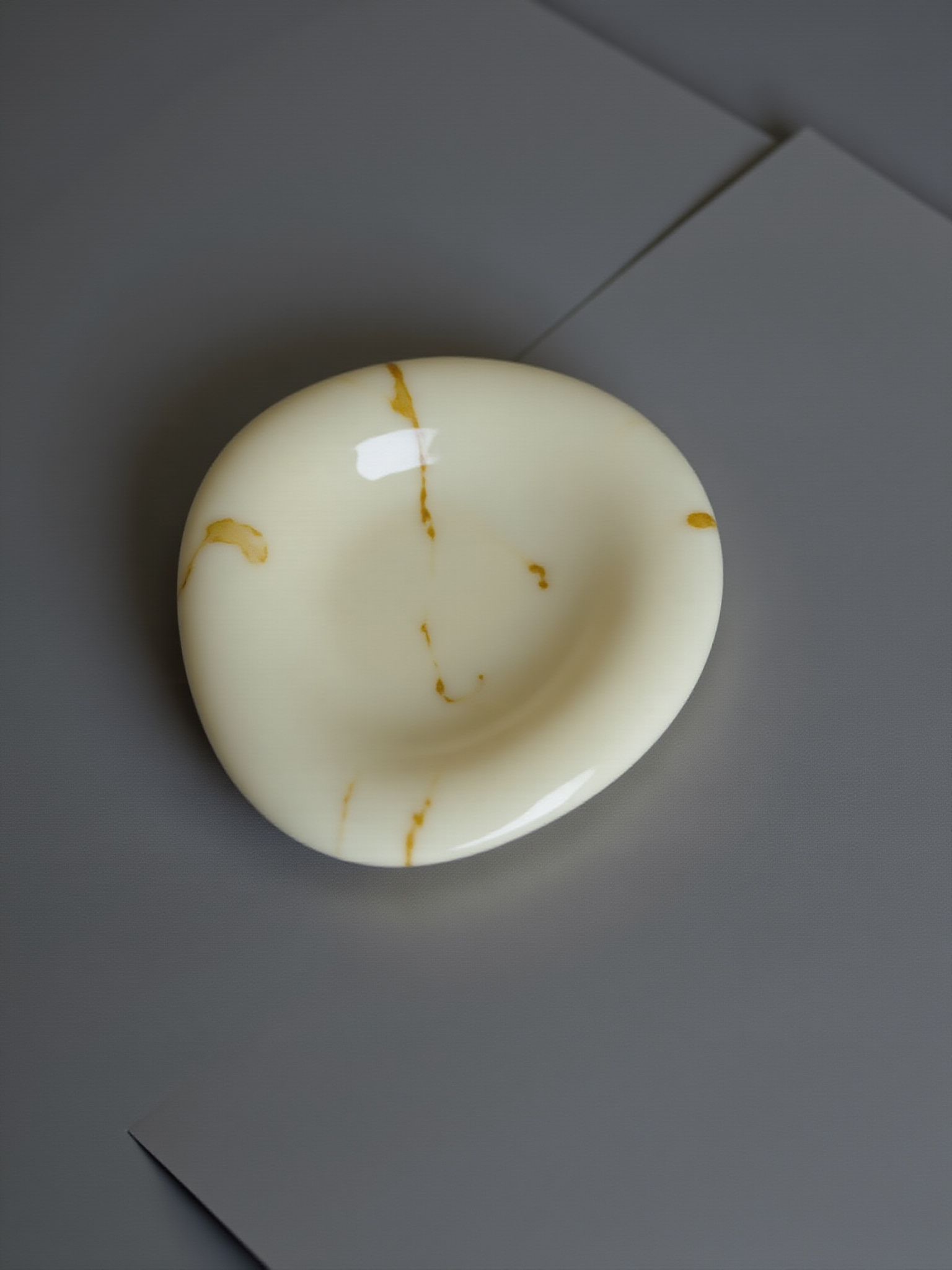 A cream paperweight with gold veining resting on a grey desk